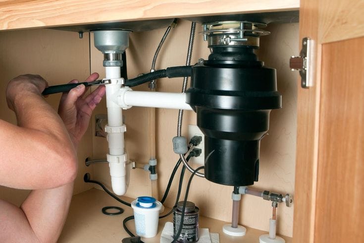 Plumber installing a garbage disposal beneath a kitchen sink in Tampa